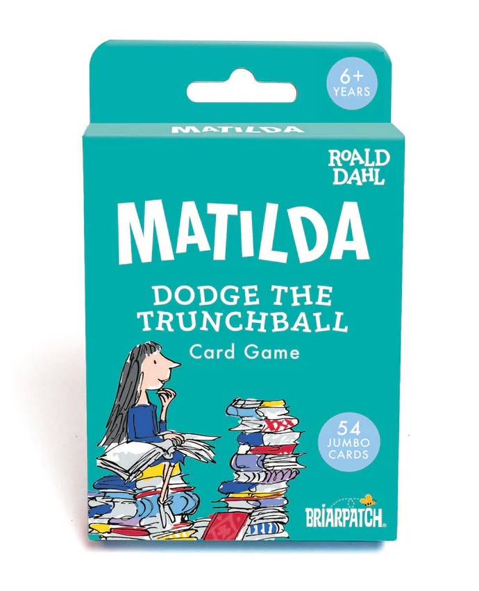 Image shows a teal-coloured packet, with a picture of a young girl sitting on top of a tall pile of books of various colours in the bottom left. She has a large book open in her lap, and another tall stack of books is in front of her. Above her in white are the words "MATILDA Dodge the Trunchball card game". At the very top, the words "6+ years" are in a blue circle, while a similar circle on the bottom right says "54 jumbo cards".